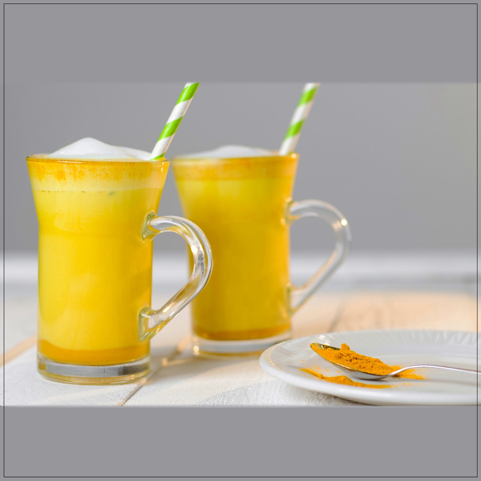 Golden milk tea in a glass mug with cinnamon and turmeric on a wooden table.