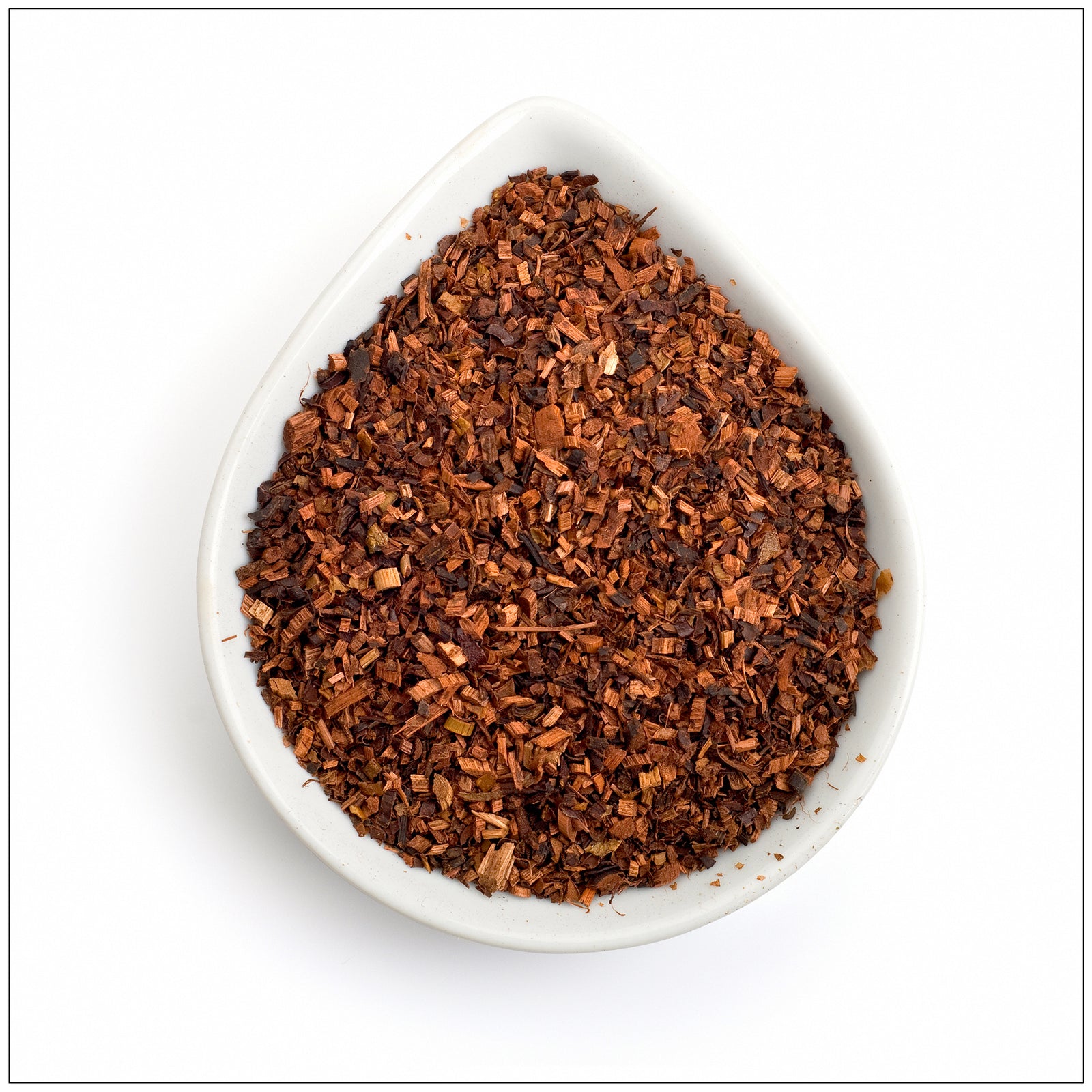 Cup of hot Honeybush tea on wooden table with dried tea leaves and fresh flowers beside it.
