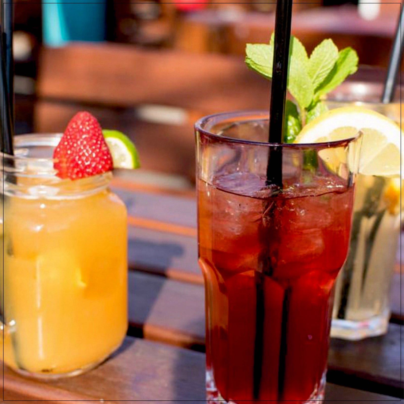 Refreshing mixed fruit tea with vibrant berries, citrus slices, and herbs in a clear glass on a wooden table.