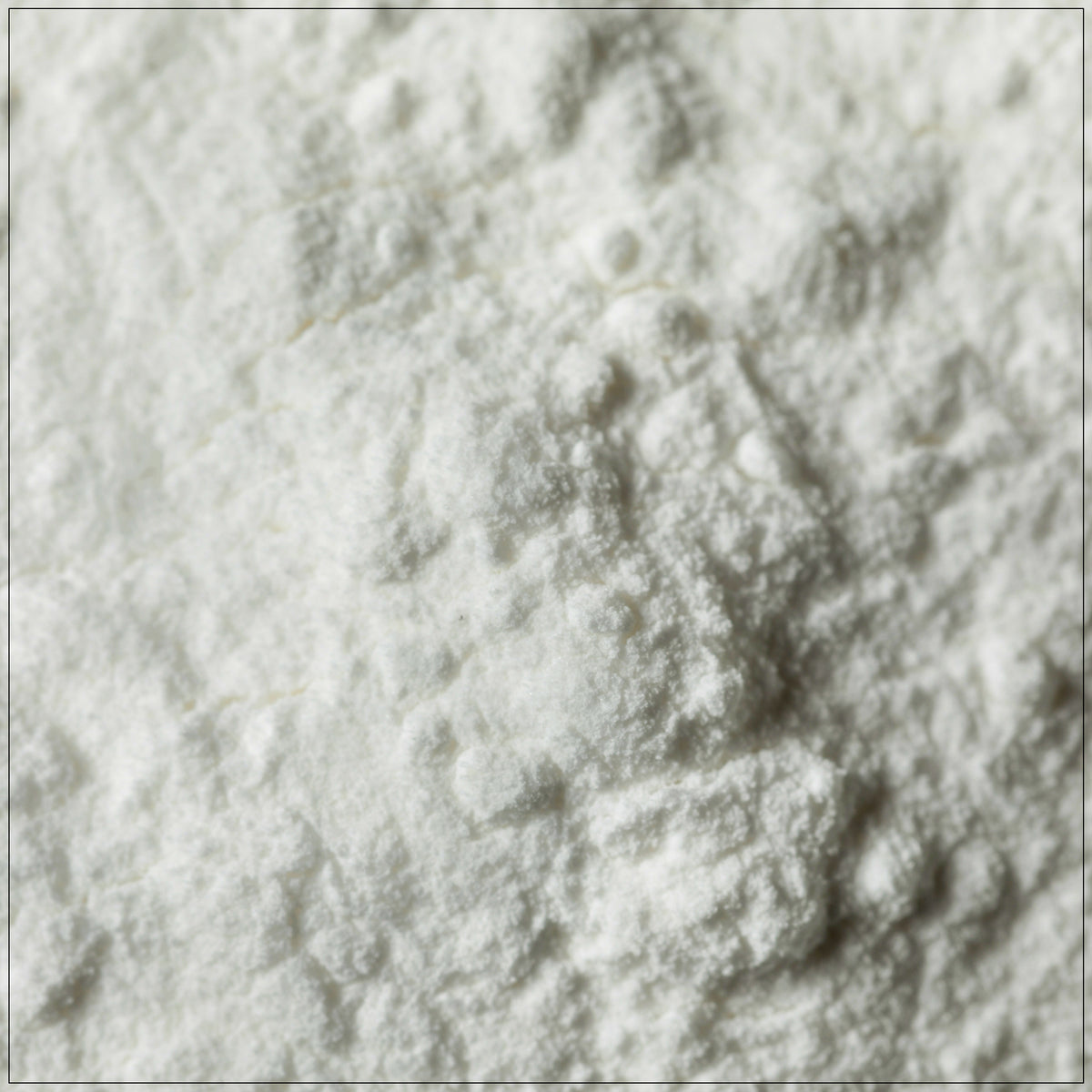 A glass jar of premium cream of tartar powder, placed on a clean kitchen counter, with a measuring spoon and fresh baked cookies in the background. Ideal for baking and stabilizing meringues.