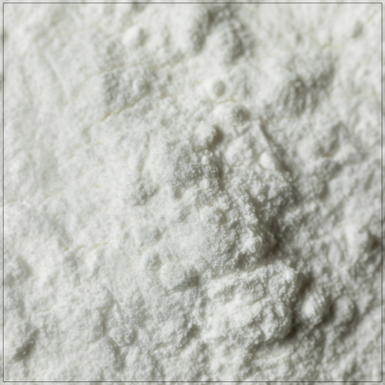 A glass jar of premium cream of tartar powder, placed on a clean kitchen counter, with a measuring spoon and fresh baked cookies in the background. Ideal for baking and stabilizing meringues.