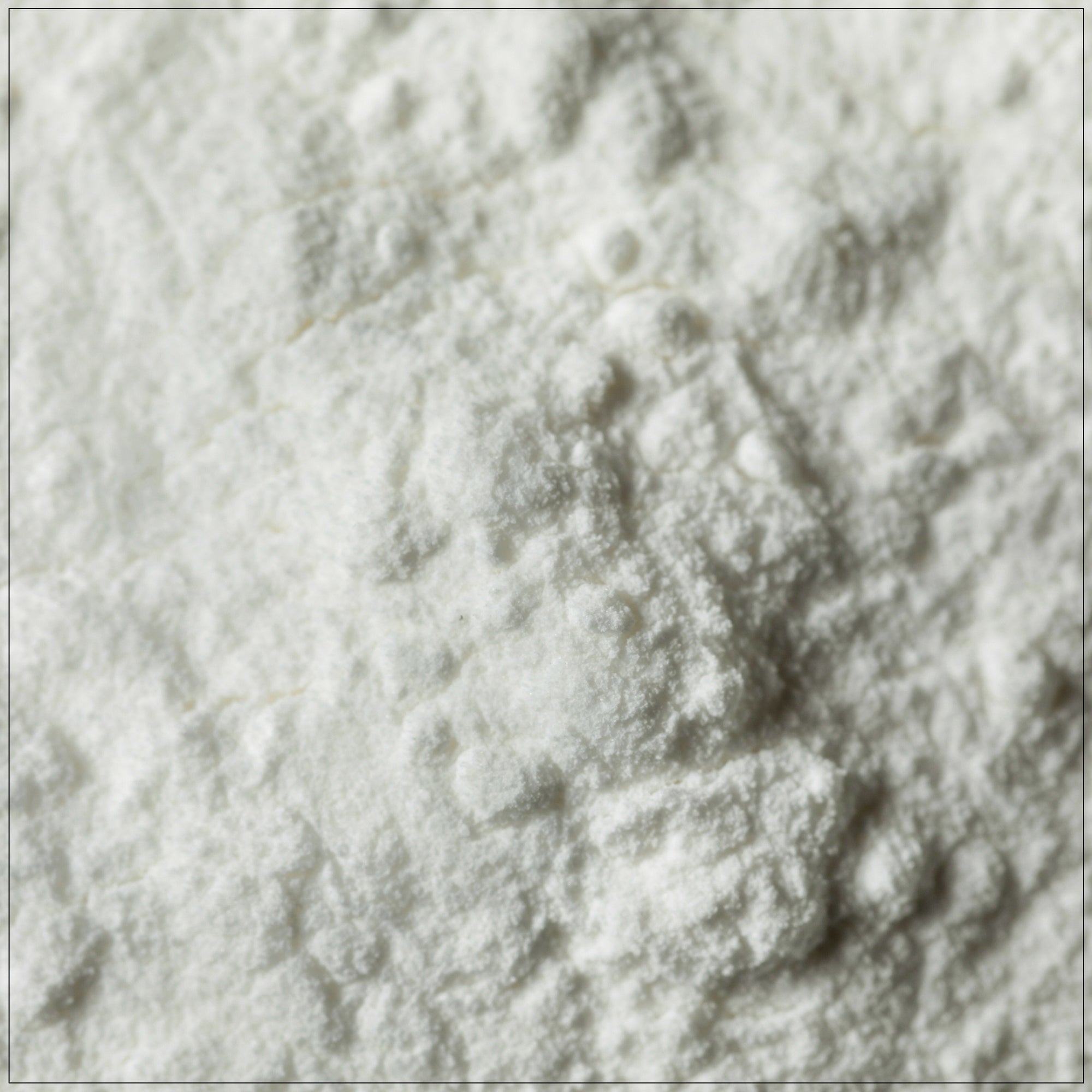 A glass jar of premium cream of tartar powder, placed on a clean kitchen counter, with a measuring spoon and fresh baked cookies in the background. Ideal for baking and stabilizing meringues.