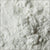 A glass jar of premium cream of tartar powder, placed on a clean kitchen counter, with a measuring spoon and fresh baked cookies in the background. Ideal for baking and stabilizing meringues.